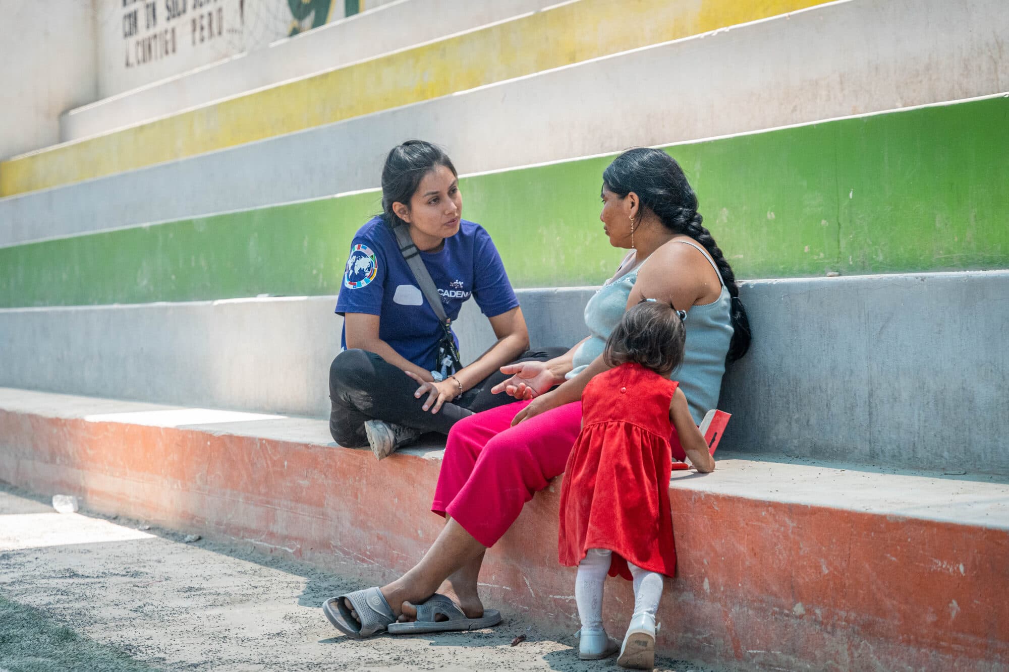 A CADENA psychologist sitting with a mother and child on steps outside