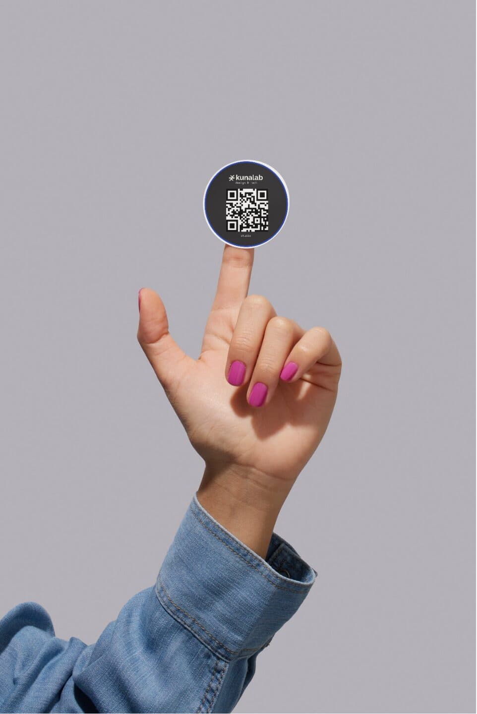 A hand balancing a Kunalab QR-code sticker on a fingertip against a grey background